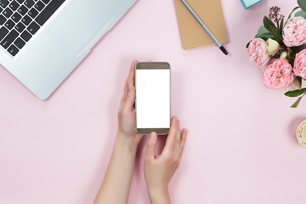 Top view of mobile phone with white copy space screen in woman hand. Flat lay of workspace