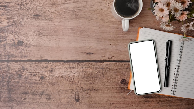 Top view mock up smart phone with white screen coffee cup and notebook on wooden table