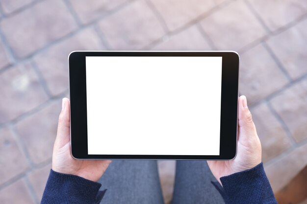 야외에 앉아있는 동안 가로로 빈 흰색 화면이 검은 태블릿 Pc를 들고 여자의 상위 뷰 모형 이미지
