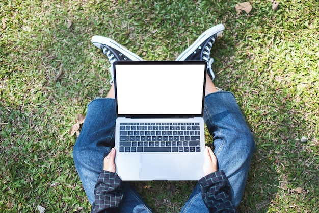 Фото Вид сверху макет изображения женщины, использующей и печатающей на ноутбуке с пустым белым экраном, сидя на открытом воздухе