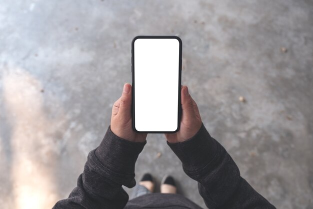 Top view mockup image of a woman holding black mobile phone with blank desktop screen while standing on concrete floor