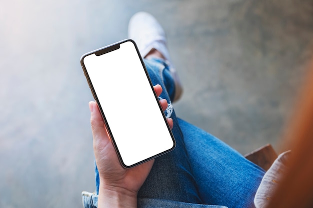 Top view mockup image of a woman holding black mobile phone with blank white screen while sitting in cafe