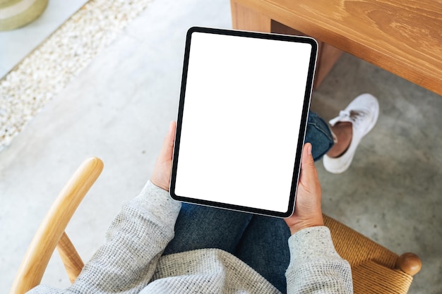 Immagine mockup vista dall'alto di una donna che tiene in mano un tablet pc nero con uno schermo desktop bianco vuoto