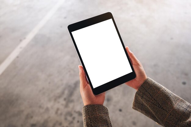 Top view mockup image of a woman holding black tablet pc with blank white screen on the street