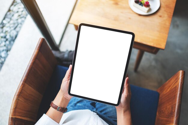 カフェで空白の白いデスクトップ画面でデジタルタブレットを保持している女性の上面モックアップ画像