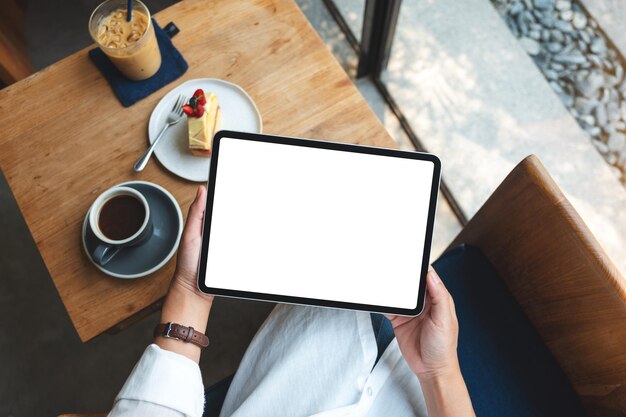 Top view mockup image of a woman holding digital tablet with blank white desktop screen in cafe