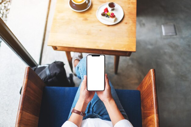 Top view mockup image of a woman holding mobile phone with blank white desktop screen in cafe