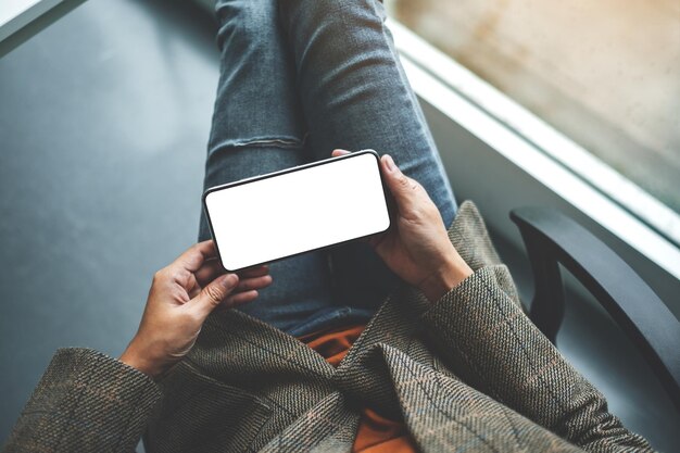 Top view mockup image of a woman holding mobile phone with blank white desktop screen