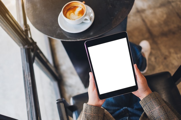 Top view mockup image of a woman sitting and holding black tablet pc with blank white desktop screen