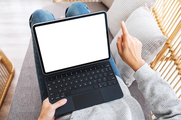 Top view mockup image of a woman using black tablet pc with blank desktop white screen as a computer pc while lying on a sofa at home