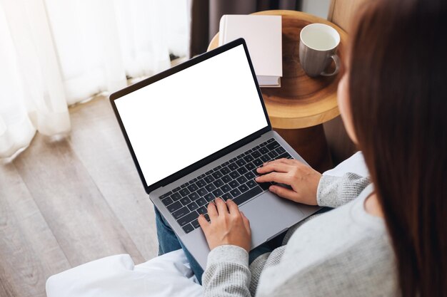 Top view mockup image of a woman working and typing on laptop computer with blank screen while sitting in bed at home