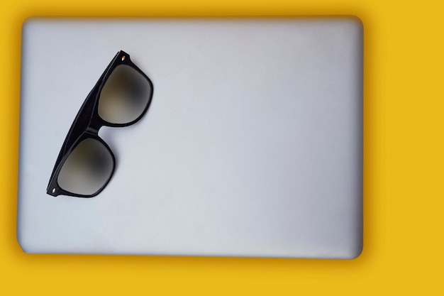 Top view of modern laptop isolated on yellow background with modern sunglasses