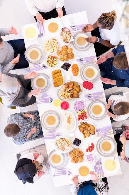 Foto vista dall'alto della moderna famiglia musulmana multietnica che prega prima di cenare insieme durante una festa del ramadan a casa