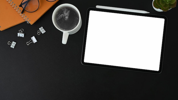Vista dall'alto della moderna scrivania da ufficio con tavoletta digitale, tazza di caffè, occhiali e notebook in pelle nera