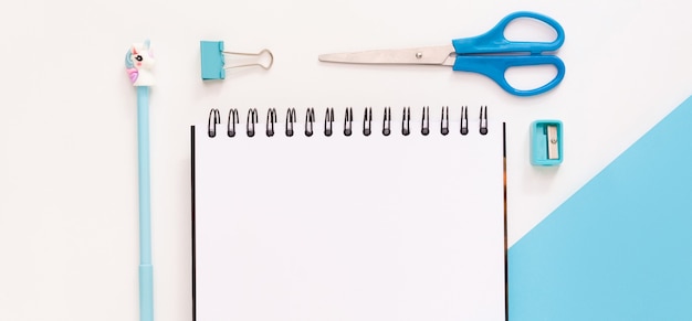 Top view of modern white blue office desktop with school supplies and stationery on table around empty space for text. Back to school concept flat lay with mockup