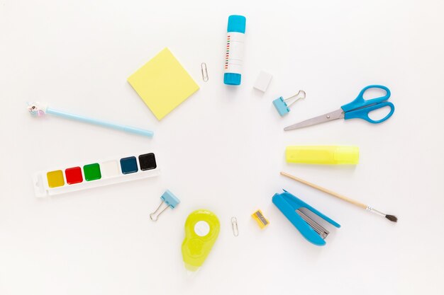 Top view of modern white blue office desktop with school supplies and stationery on table around round empty space for text. Back to school concept flat lay with mockup