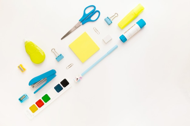 Top view of modern white, blue, yellow office desktop with school supplies and stationery on table around diagonal empty space for text. Back to school concept flat lay with mockup