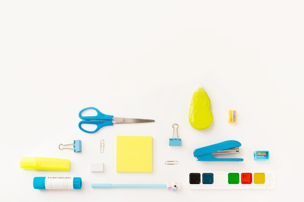 Top view of modern white, blue, yellow office desktop with school supplies and stationery on table around diagonal empty space for text. Back to school concept flat lay with mockup