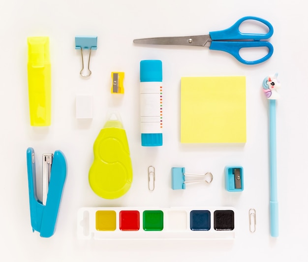 Top view of modern white, blue, yellow office desktop with school supplies and stationery on table around empty space for text. Back to school concept flat lay with mockup