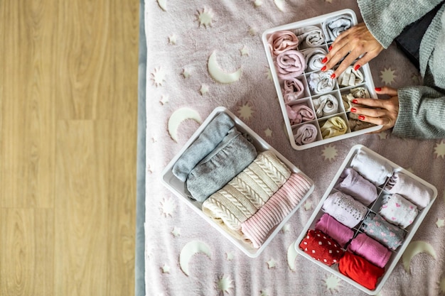 Vista dall'alto delle mani della madre che mettono ordinatamente i vestiti del bambino femminile in una custodia di plastica comoda per riporre i vestiti