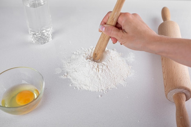 白いテーブル生地にガラス木のスプーン水めん棒で小麦粉卵をマウンドのトップ ビュー