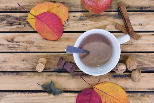 Top view on a mug full of chocolate drink among red leaf on wooden background