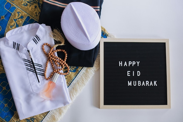 Top view of Muslim traditional dress and prayer beads on the prayer mat with letter board says Happy Eid Mubarak