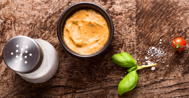 Photo top view of mustard in bowl with salt shaker and tomato