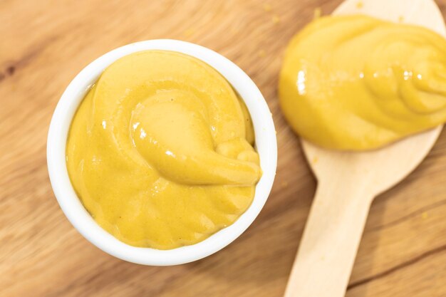 Photo top view of mustard sauce in bowl and spoon on wooden table