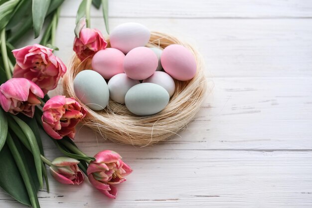 Top view of a nest with eggs in gentle pastel colors and a bouquet of tulips on a white background