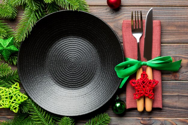 Top view of New Year dinner on festive wooden background. Composition of plate, fork, knife, fir tree and decorations. Merry Christmas 