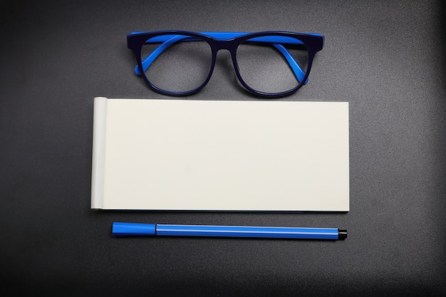 Top view note paper with blue eye glasses and blue pen on dark background