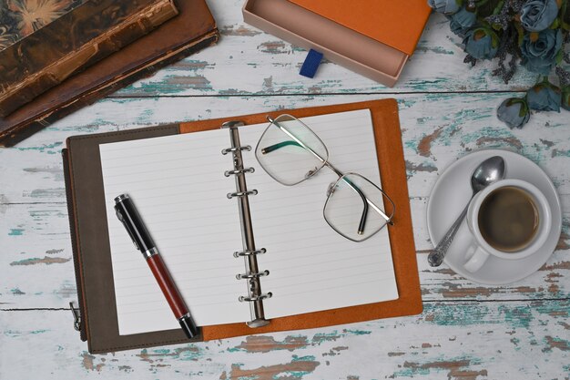 Top view notebook, glasses and coffee cup on wooden table.