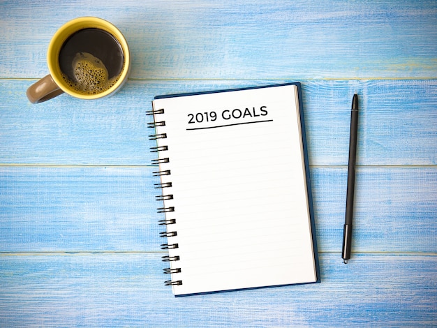 Top view of notebook handwriting goals 2019 year on blue wooden table. 