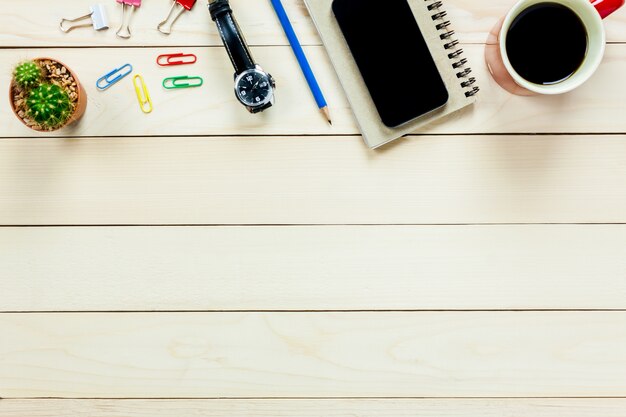 Top view notebook,pencil,black coffee,cactus, watch,mobile phone,paperclips on office desk background.