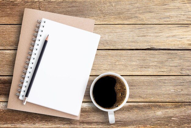 Top view of notebook pencil and cup of coffee on wood table background