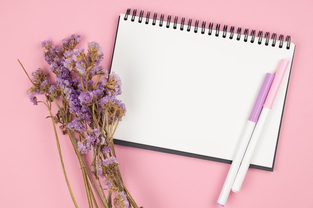 Top view of notebook and violet flower on pink table