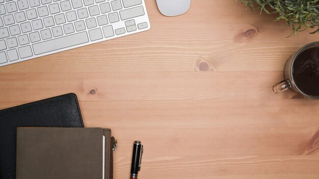 Top view notebooks, coffee cup, keyboard and houseplant on wooden table.