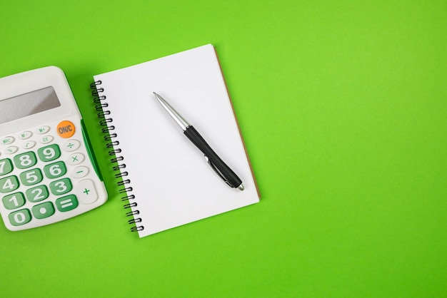 Top view of notepad with pen and calculator on green background copy space