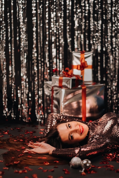 Фото Вид сверху девушки, лежащей в блестящей одежде на полу в конфетти в виде сердечек и подарков.