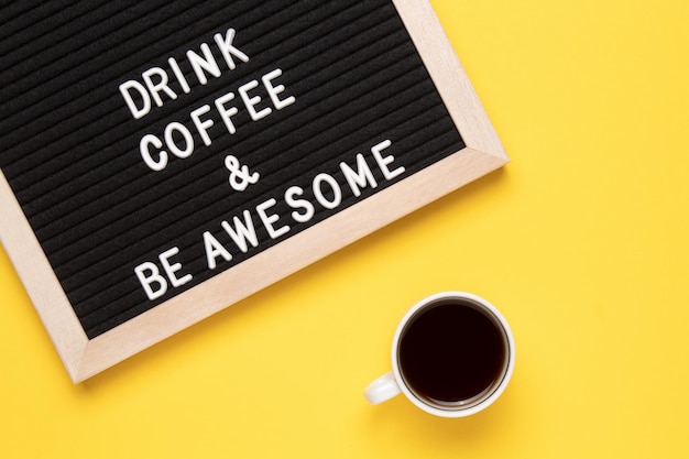Фото Вид сверху на чашку черного кофе и фразу пить кофе и быть потрясающим на доске объявлений