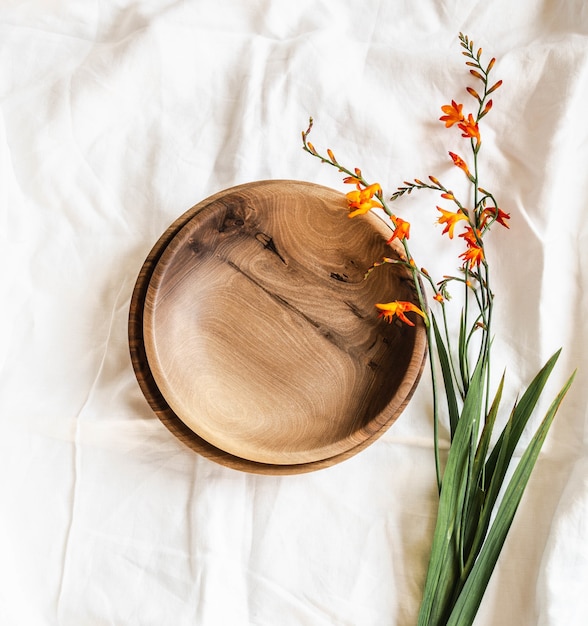 写真 空の茶色の丸い手作りの木製ボウルと白い綿のテーブルクロスにオレンジ色の花の上面図。フラットレイ。コピーsapce