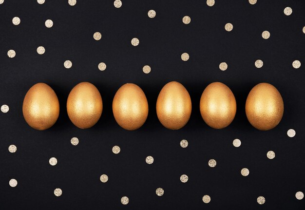 Фото Верхний вид золотистых пасхальных яиц в ряду и конфети на темно-черном фоне