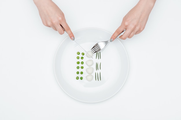 사진 포크와 나이프를 사용하여 녹색 완두콩, 모짜렐라, 허브를 먹는 젊은 여자의 손의 상위 뷰