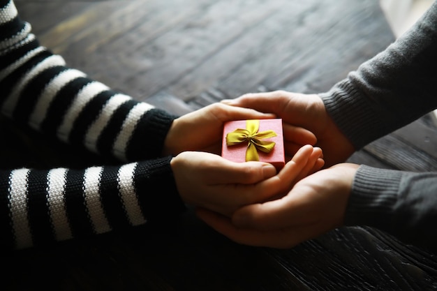 写真 木製の背景にリボン付きギフト ボックスを保持している男性と女性の手の平面図誕生日バレンタインデー クリスマス新年おめでとう背景コピー スペースに存在します。