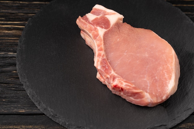 Фото Взгляд сверху цельных сырцовых стейков свиной отбивной на черной каменной разделочной доске.