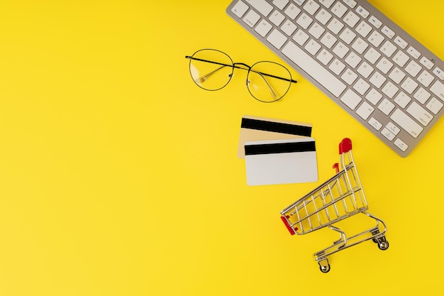 Фото Верхний вид концепции онлайн-покупок с корзиной кредитной карты и компьютером, изолированным на желтом фоне