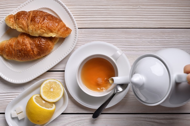 白いテーブルにレモンとクロワッサンのカップにお茶を注ぐのトップビュー