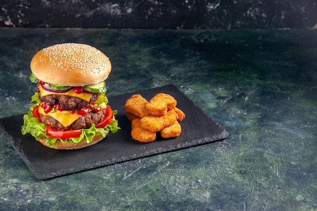 어두운 색상 트레이에 녹색 토마토와 검은 색 표면의 오른쪽에 치킨 너겟과 함께 맛있는 고기 샌드위치의 상위 뷰