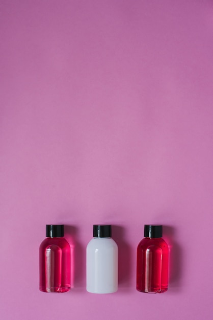 ピンクの背景の上に白と深紅色の3つの小さなボトルと体と髪のケア製品のトップビュー